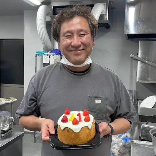 誕生日ケーキを持って笑顔を見せる理事長